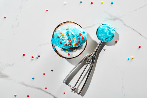 top view of fresh blue ice cream with sprinkles on coconut half and in ice cream spoon on marble grey background