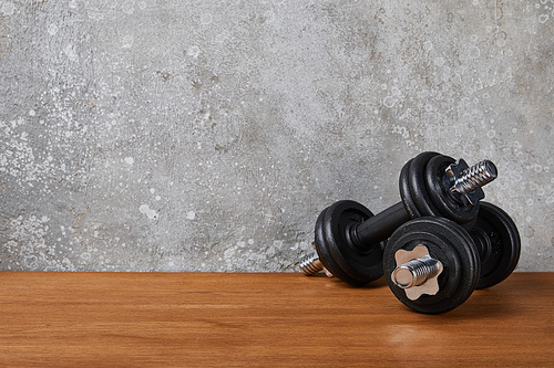 heavy and black dumbbells on wooden surface near concrete wall