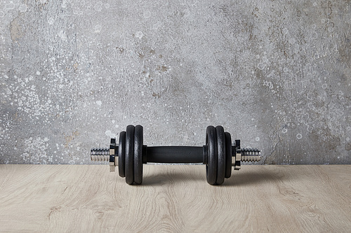 heavy and black dumbbell on wooden surface near concrete wall