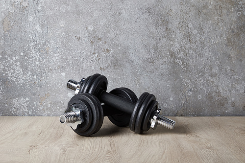heavy dumbbells on wooden surface near concrete wall