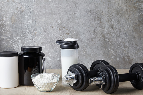 dumbbells near protein shake in sports bottle and protein powder near concrete wall