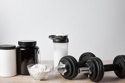 protein shake in sports bottle near jars and dumbbells on white