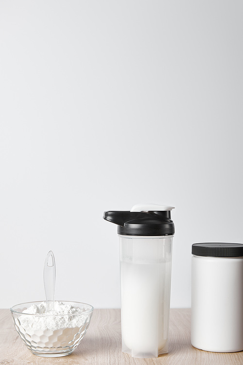 protein shake in sports bottle near jar and glass bowl with protein shake isolated on grey