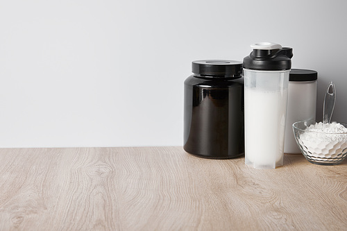 protein shake in sports bottle near jars and glass bowl with protein powder isolated on grey