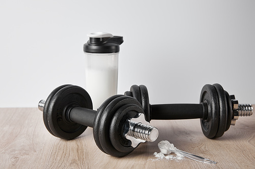 spoon with protein powder near dumbbells and sports bottle isolated on grey