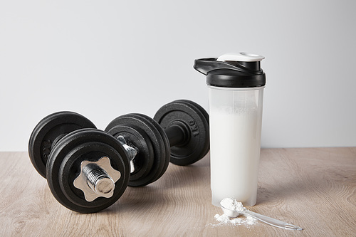 spoon with protein powder near black dumbbells and sports bottle isolated on grey