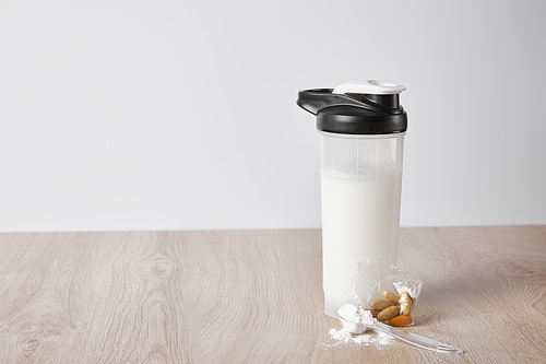 sports bottle with protein shake near almonds isolated on grey