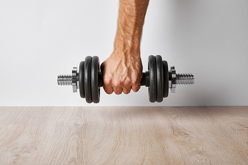 cropped view of sportsman holding dumbbell on white