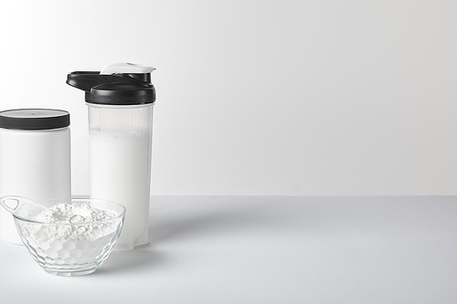 sports bottle with protein shake near jar and protein powder on white