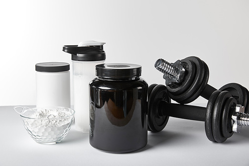 heavy dumbbells near jars and sports bottle with protein shake on white