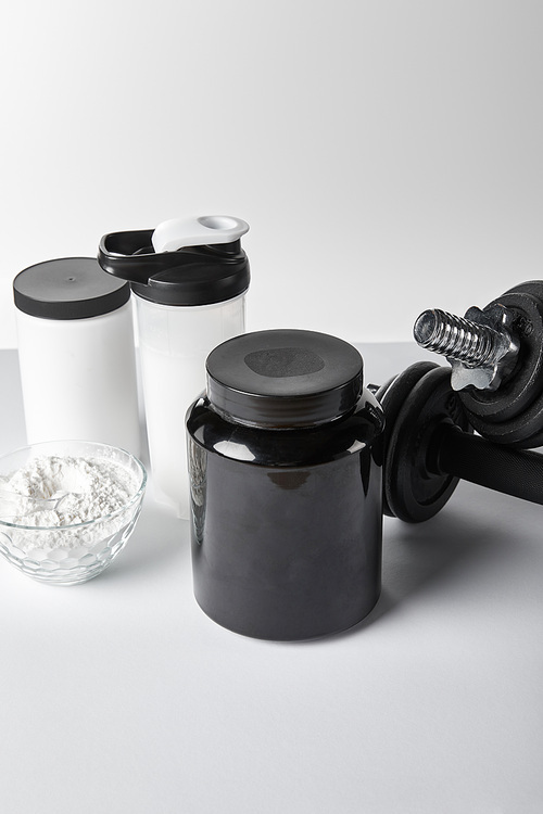 jars and sports bottle near bowl with protein powder on white