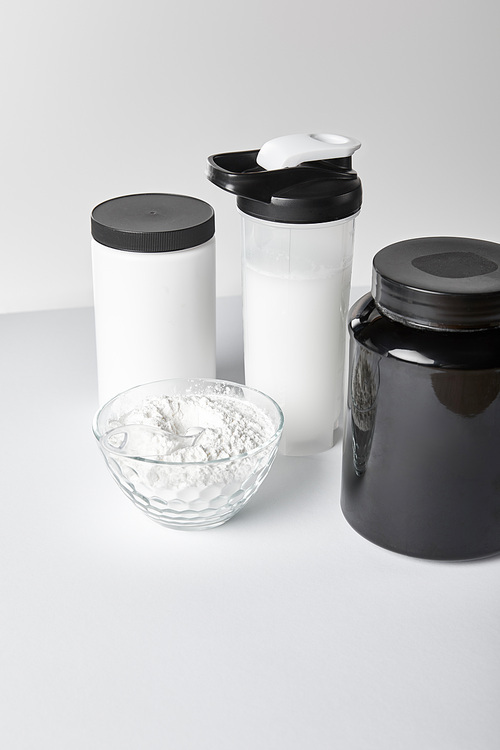jars and sports bottle with protein shake near bowl with protein powder on white