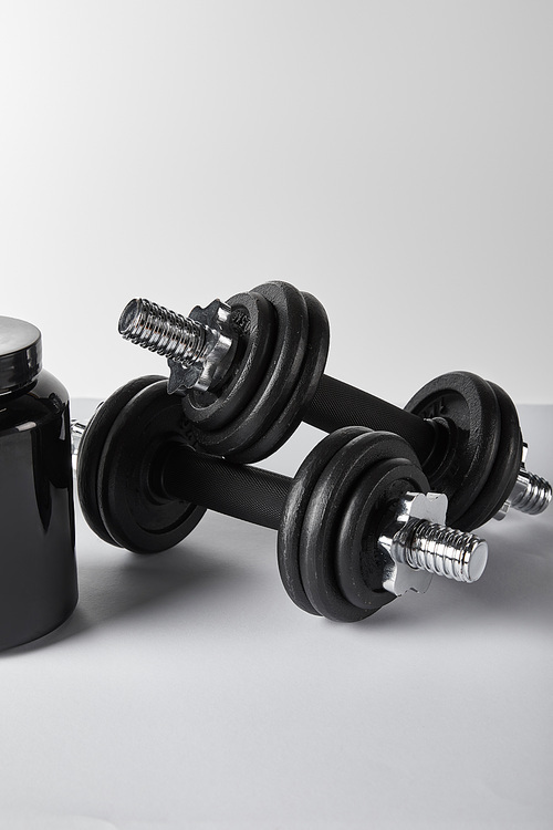 black jar with protein near heavy dumbbells on white
