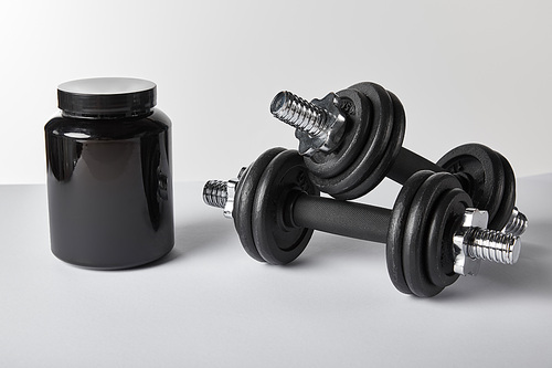 black jar with protein near dumbbells on white