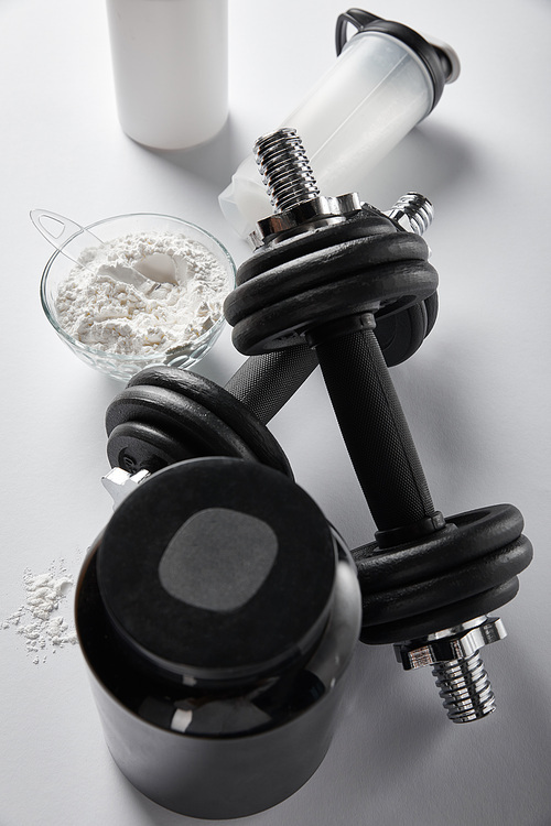 top view of sports bottle near bowl with protein powder and dumbbells on white