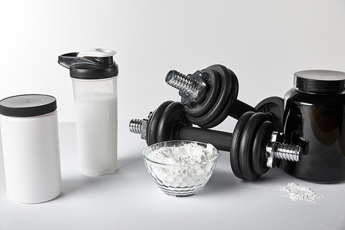 jars and sports bottle near bowl with protein powder and dumbbells on white