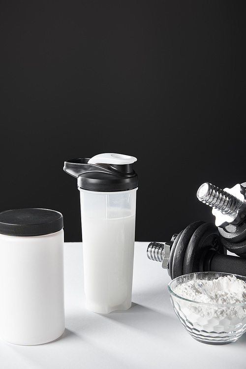 glass bowl with protein powder near dumbbells and sports bottle on black