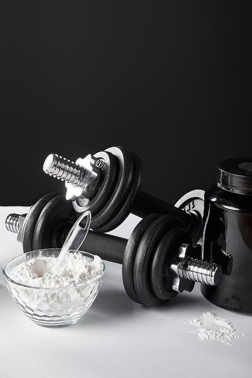 glass bowl with protein powder near dumbbells on black
