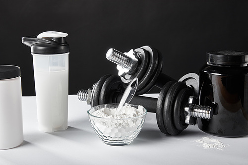 glass bowl near sports bottle with protein shake on black