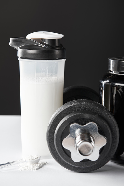 spoon with protein near dumbbell and sports bottle with protein shake on black