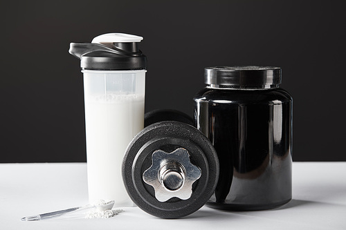 spoon near dumbbell and sports bottle with protein shake on black