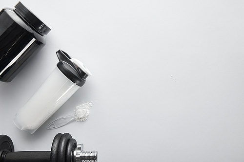 top view of spoon with protein near dumbbell, jar and sports bottle on white