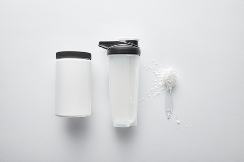 top view of jar near spoon with protein and sports bottle on white