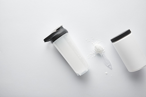 top view of jar near sports bottle and spoon with protein on white