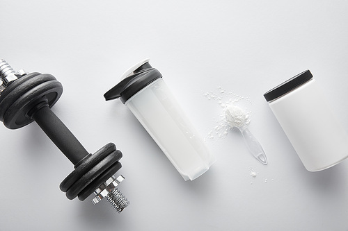 top view of spoon with protein near dumbbell and sports bottle on white