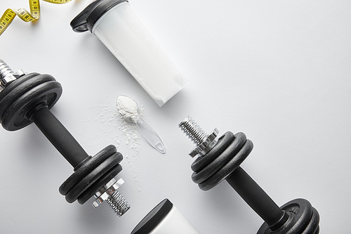 top view of spoon with protein powder near heavy dumbbells and sports bottle on white