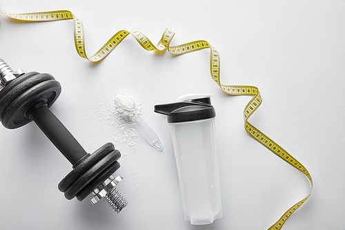 top view of measuring tape near dumbbell and sports bottle on white