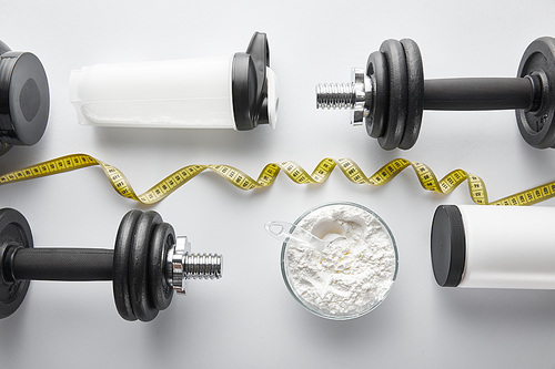 top view of heavy dumbbells near sports bottle and measuring tape on white