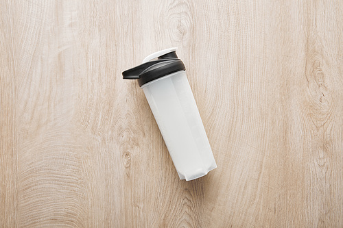 top view of sports bottle with protein shake on wooden surface