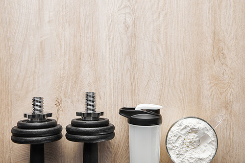 top view of heavy dumbbells near sports bottle and jar on wooden surface