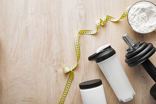 top view of heavy dumbbell near sports bottle and measuring tape on wooden surface