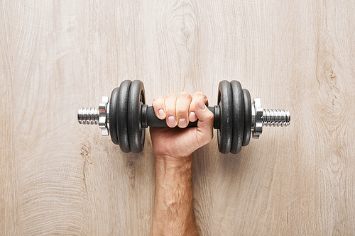 top view of sportsman holding dumbbell near wooden surface