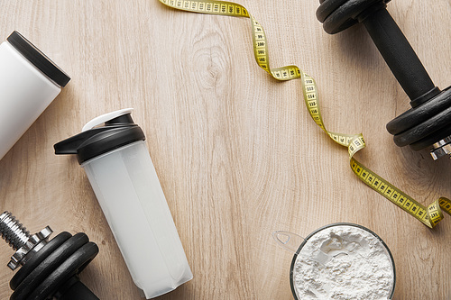 top view of dumbbells near sports bottle and measuring tape on wooden surface