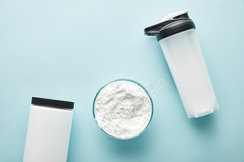 top view of sports bottle near jar and glass bowl with protein powder on blue