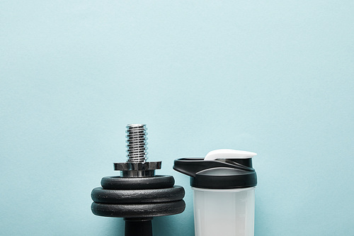 top view of dumbbell near sports bottle with protein shake on blue