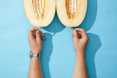 cropped shot of human hands and halved ripe  on blue