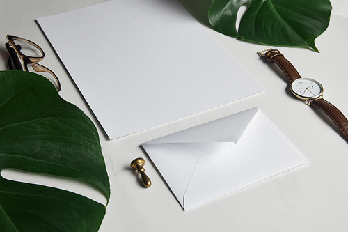 Business mock up set with envelope and watch on white marble background with monstera leaves
