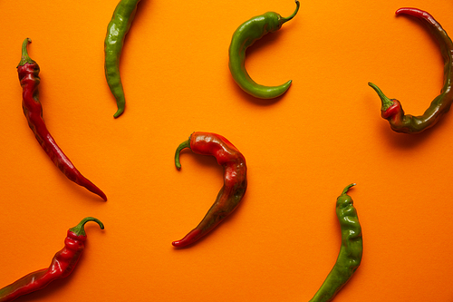 top view of fresh green and red chili peppers on orange background
