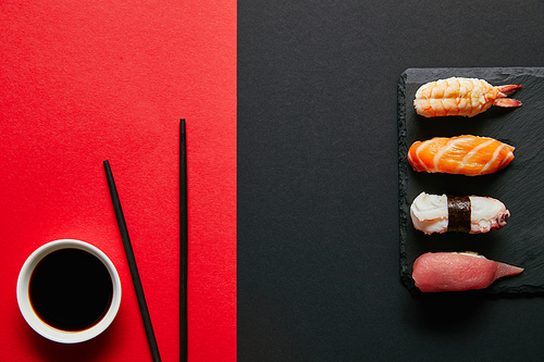 flat lay with soya sauce in bowl| chopsticks and nigiri sushi set on black slate plate on red and black background