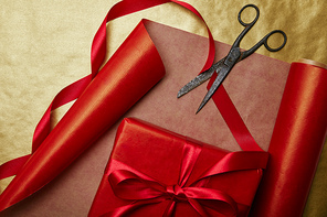 top view of wrapped gift| ribbons and scissors on red and golden wrapping paper background