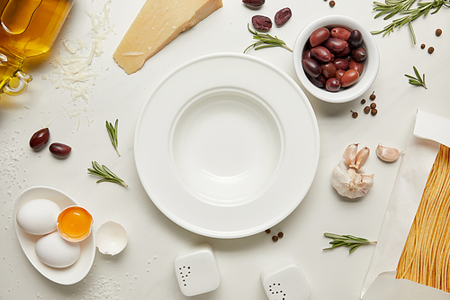 flat lay with empty plate and pasta ingredients on white marble surface