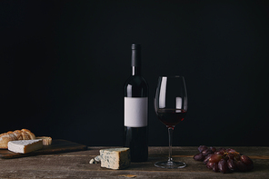 bottle of wine with blank label| glass of red wine| cheese and grapes on wooden table