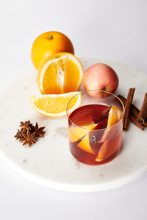 close up view of hot mulled wine in glass| spices| oranges and apple on white tabletop
