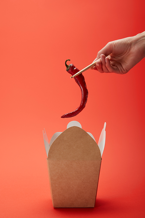 cropped image of woman holding chili pepper in chopsticks above noodle box on red