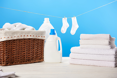 laundry basket| plastic containers with laundry liquids| pile of clean soft towels and white socks hanging on rope on blue