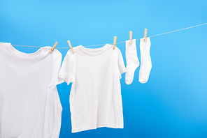 clean white t-shirts and socks hanging on clothesline isolated on blue